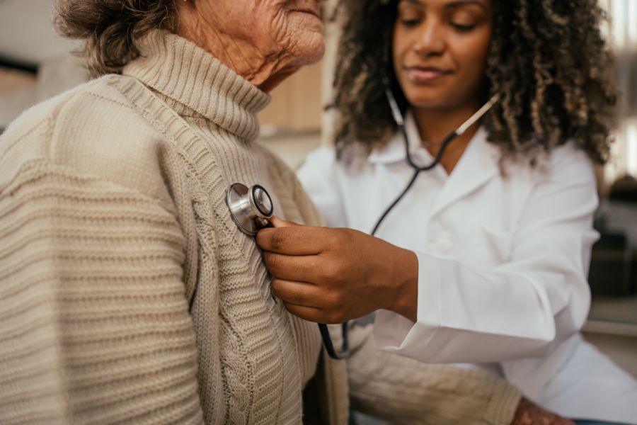 Healthcare professional listening to elderly woman's heart with stethoscope at home - home consultation
